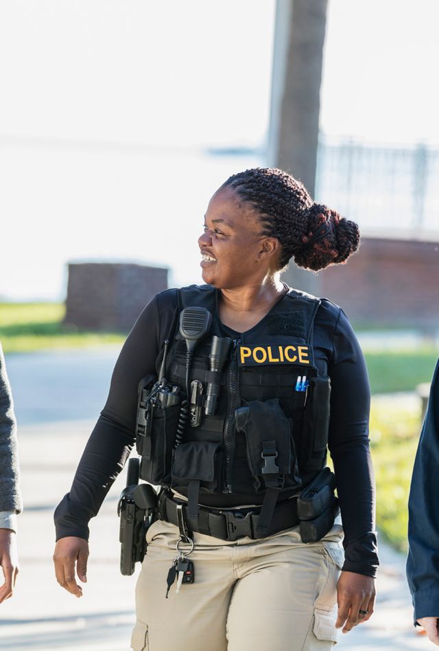 Community policing - a female police officer walking and conversing with two adolescents. The African-American boy is a 14 year old teenager. His friend is 12 years old. The policewoman is a mature African-American woman in her 40s.