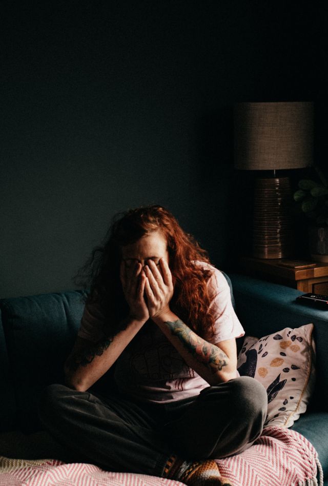 A woman sitting cross-legged on a couch with her head in her hands