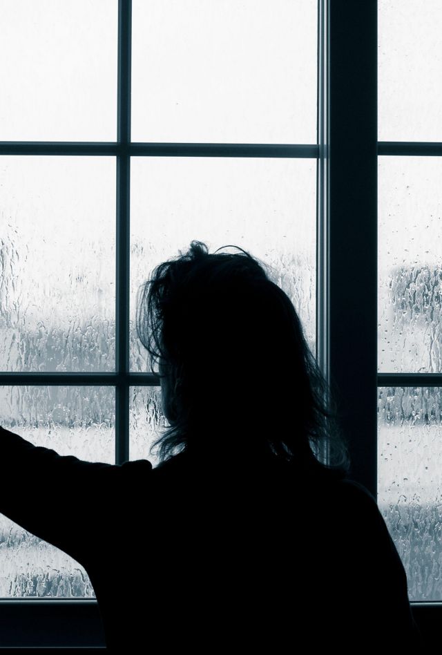 2B7JCT1 Woman looking out of window on rainy day. Conept image; female depression, domestic abuse, self isolation, quarantine, Coronavirus,