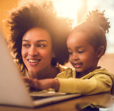 Mother and young daughter smiling while using laptop