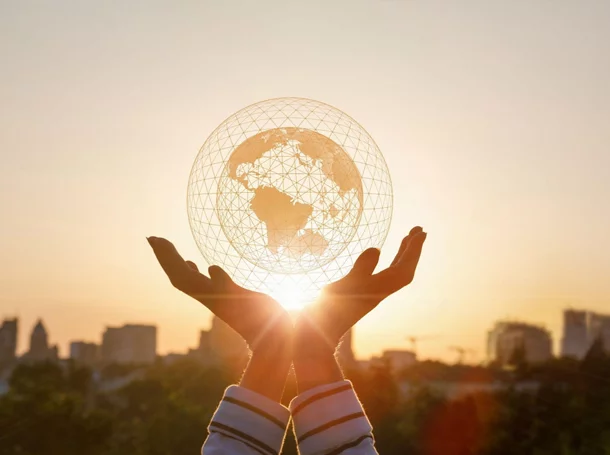 Two hands holding a globe in front of a sunrise