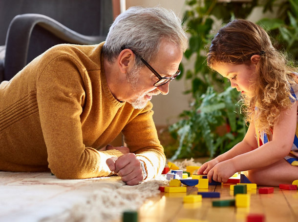 Une petite-fille joue avec des blocs en bois sous le regard de son grand-père