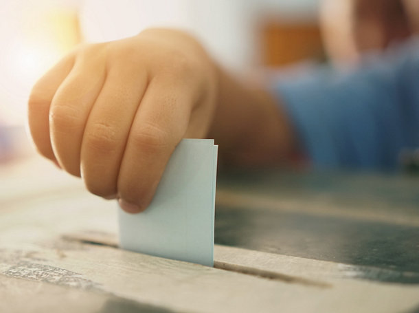 Close-Up Of Hand Inserting Paper In Ballot Box