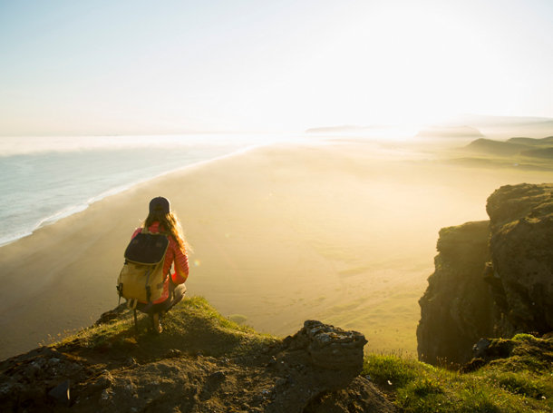 A woman standing on a cliff edge at sunset in Iceland.