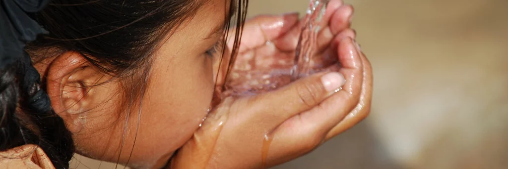 Petit enfant aux cheveux noirs buvant de l'eau à l'aide de ses mains