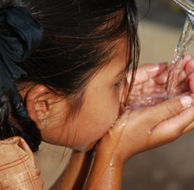 Petit enfant aux cheveux noirs buvant de l'eau à l'aide de ses mains