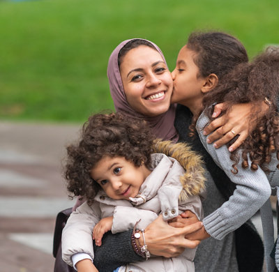Muslim mother hugging daughters in city park
