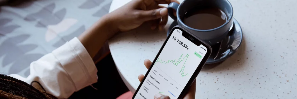 Phone displaying investment trading app next to a cup of coffee. 
