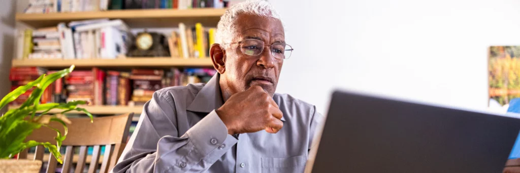 Person sitting at a desk working on a laptop in a room with bookshelves in the background.