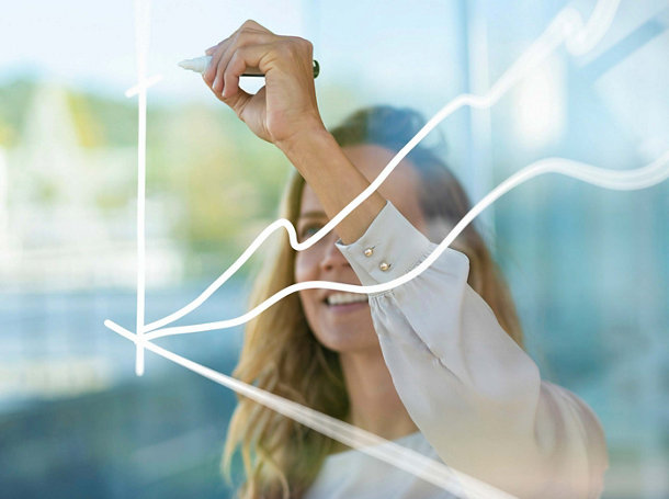 Businesswoman drawing graph on glass while standing at modern office