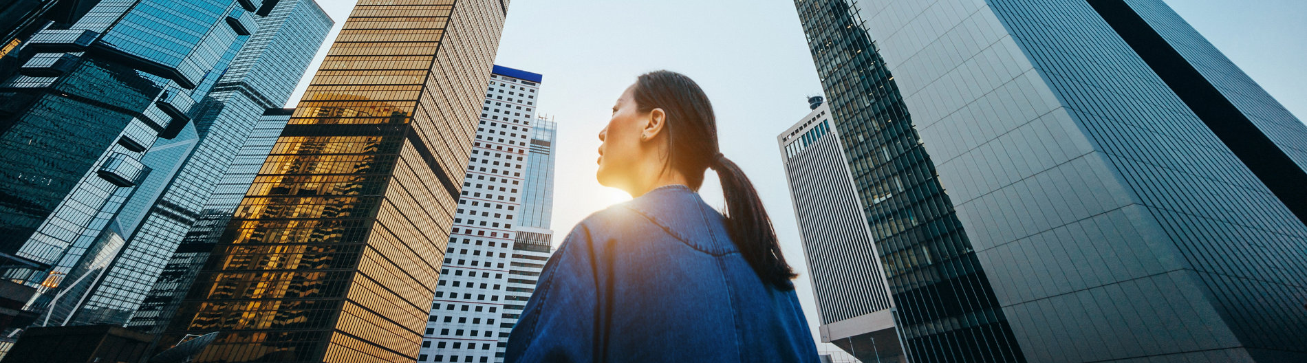 Vue en contrebas d’une femme debout devant des gratte-ciel modernes et un ciel bleu au lever du soleil, en ville.