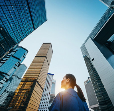 Low angle view of woman standing against modern skyscrapers and blue sky in city at sunrise