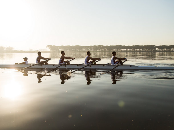 Mixed race rowing team training on a lake at dawn