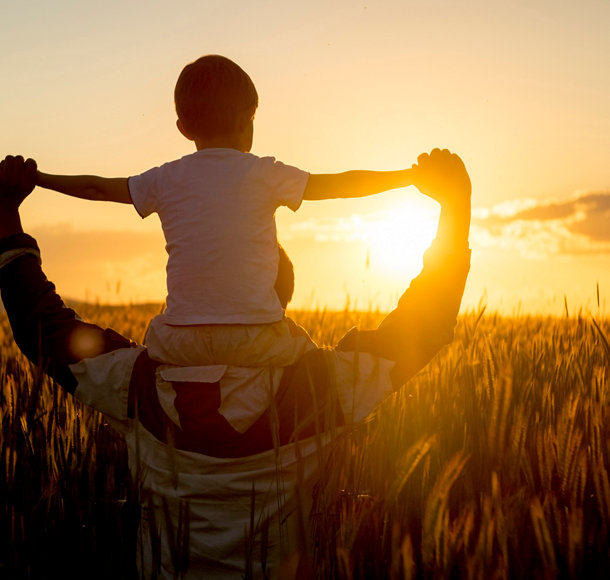 Un père porte son fils sur ses épaules dans un champ de blé au coucher du soleil.