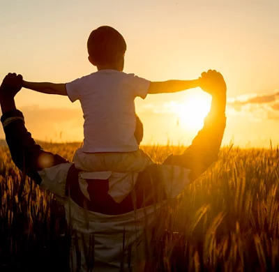 Father carrying son on shoulders in field of wheat at sunset