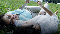 Two people laying in the grass holding paper cutouts of a house