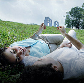 Two people laying in the grass holding paper cutouts of a house