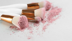 Different makeup brushes with crushed cosmetic product on light background