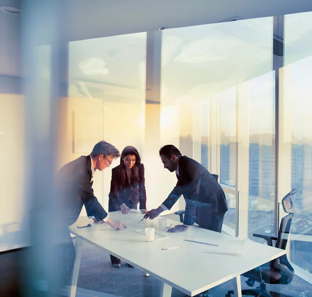 three people standing around a desk in an office setting