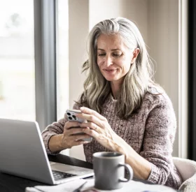 Mature woman uses her phone while sitting at her dining room table