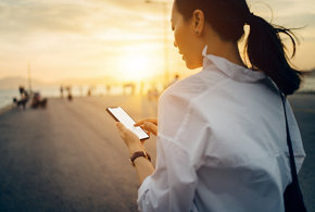 Une jeune femme utilise un téléphone intelligent en faisant une promenade relaxante près d’un quai au coucher du soleil