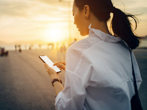 A young woman browsing on a smartphone while walking in the evening breeze