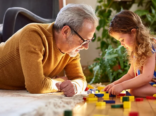 Granddaughter playing with wooden block and granddad watching