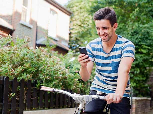 A man laughing at his smartphone while riding a bicycle