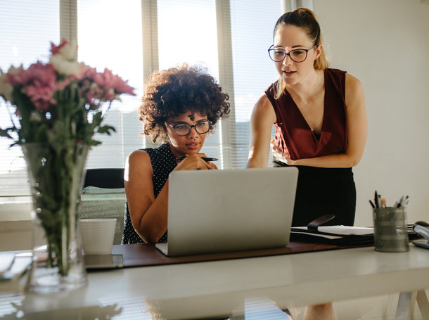 Deux jeunes femmes au bureau discutent d’un projet devant un ordinateur portable. Des collègues de travail discutent devant un bureau sur lequel est placé un ordinateur portable.
