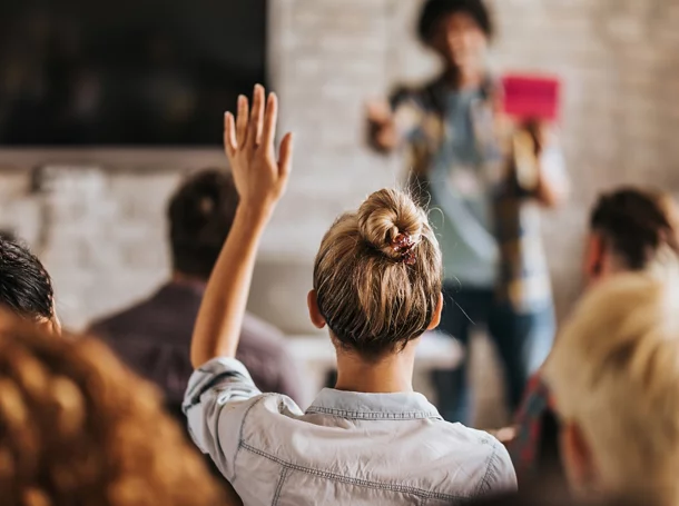 Back view of a woman raising her hand to ask a question during a seminar