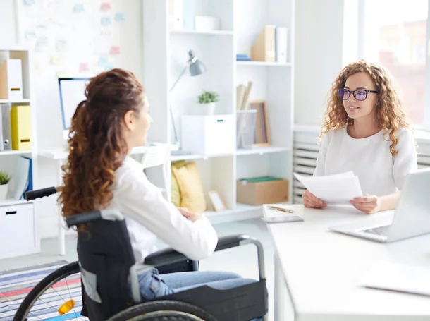 Un jeune employeur et une femme en fauteuil roulant sont assis l’ un devant l’autre et discutent pendant une entrevue.