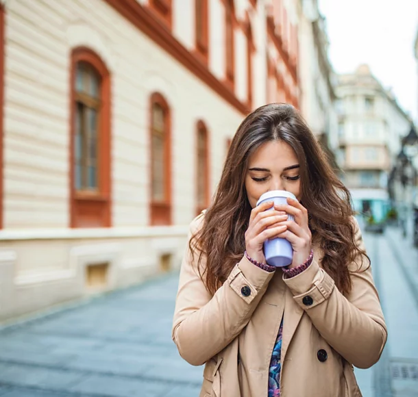 Une belle femme marche près d’un immeuble de bureaux avec un café pour se rendre au travail.