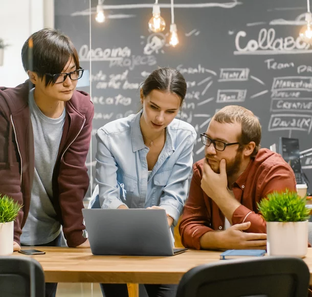 Trois personnes créatives discutent activement de projets en cours en utilisant un ordinateur portable. De jeunes gens élégants travaillent dans un environnement tendance.