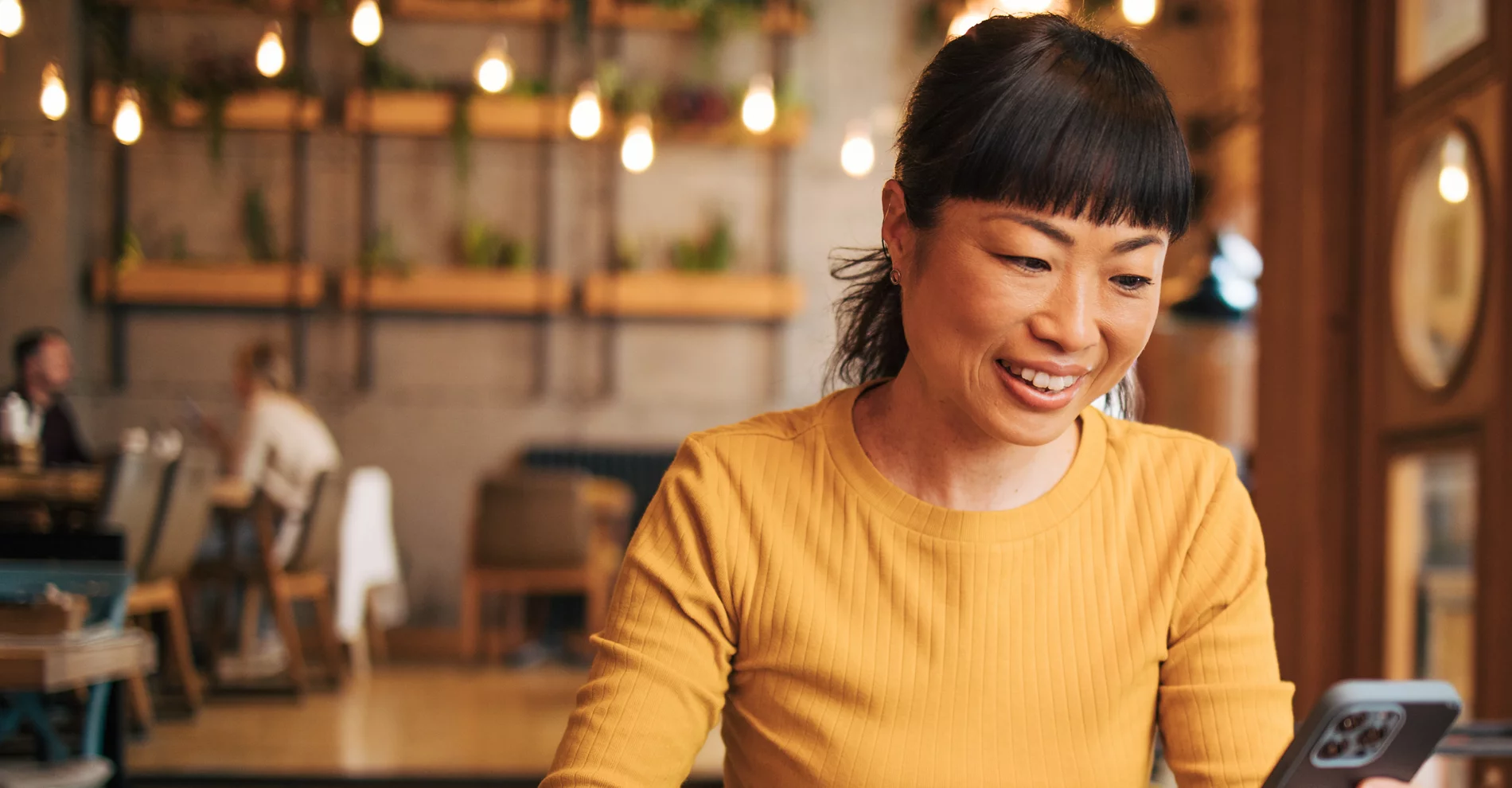 Une femme souriante dans un café regarde son cellulaire