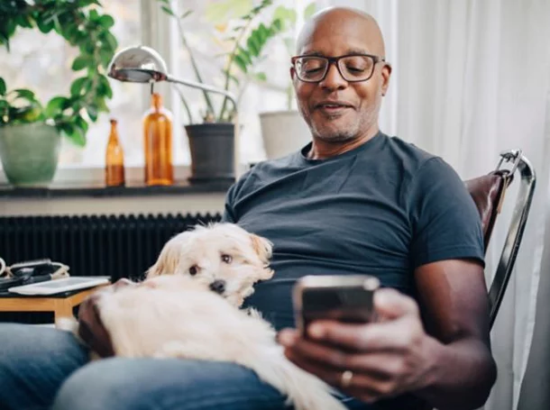 Image of a man with a dog on his lap holding his phone and smiling while looking at his phone