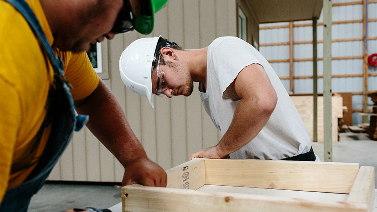Two construction workers build a wooden frame.