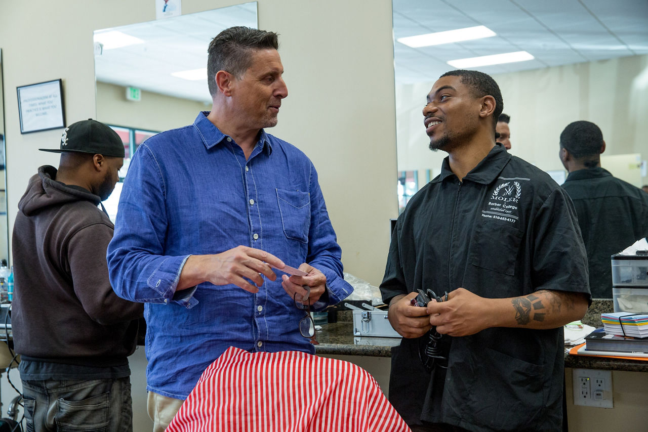 Frank Quattro, owner of Moler Barber College, speaking with Jamon Smallwood, a student. Another student, Menyoli Westbrook, looks on. To get people into jobs that pay a living wage, the San Pablo Economic Development Council partners with groups that teach skills, such as haircutting at the Moler Barber College.
