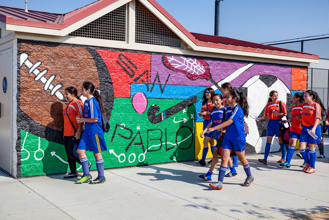 Mural with youth soccer players at Rumrill Sports Park. At the new Rumrill Sports Park in an industrial part of San Pablo, soccer teams face off on three new fields with artificial turf and field lights. San Pablo has the highest childhood obesity rate in the county — but the least amount of park and open space. The city and San Pablo Economic Development Corp. worked with federal and state agencies to rehabilitate vacant railroad land, then raised funds through the federal New Market Tax Credit program to build state-of-the-art fields. “We did not have a safe, lit, lined, turfed field anywhere around here. The nearest one is in Berkeley,” says Leslay Choy, general manager of the San Pablo Economic Development Corp.