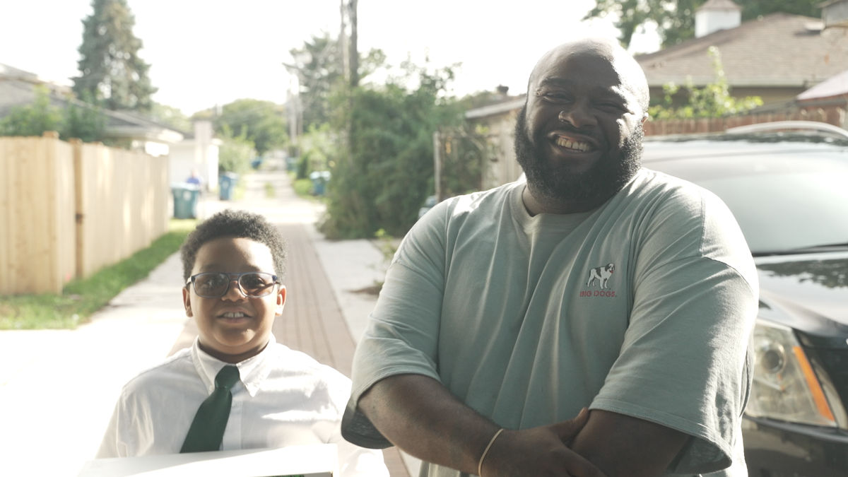A man and young boy stand together outside smiling. 