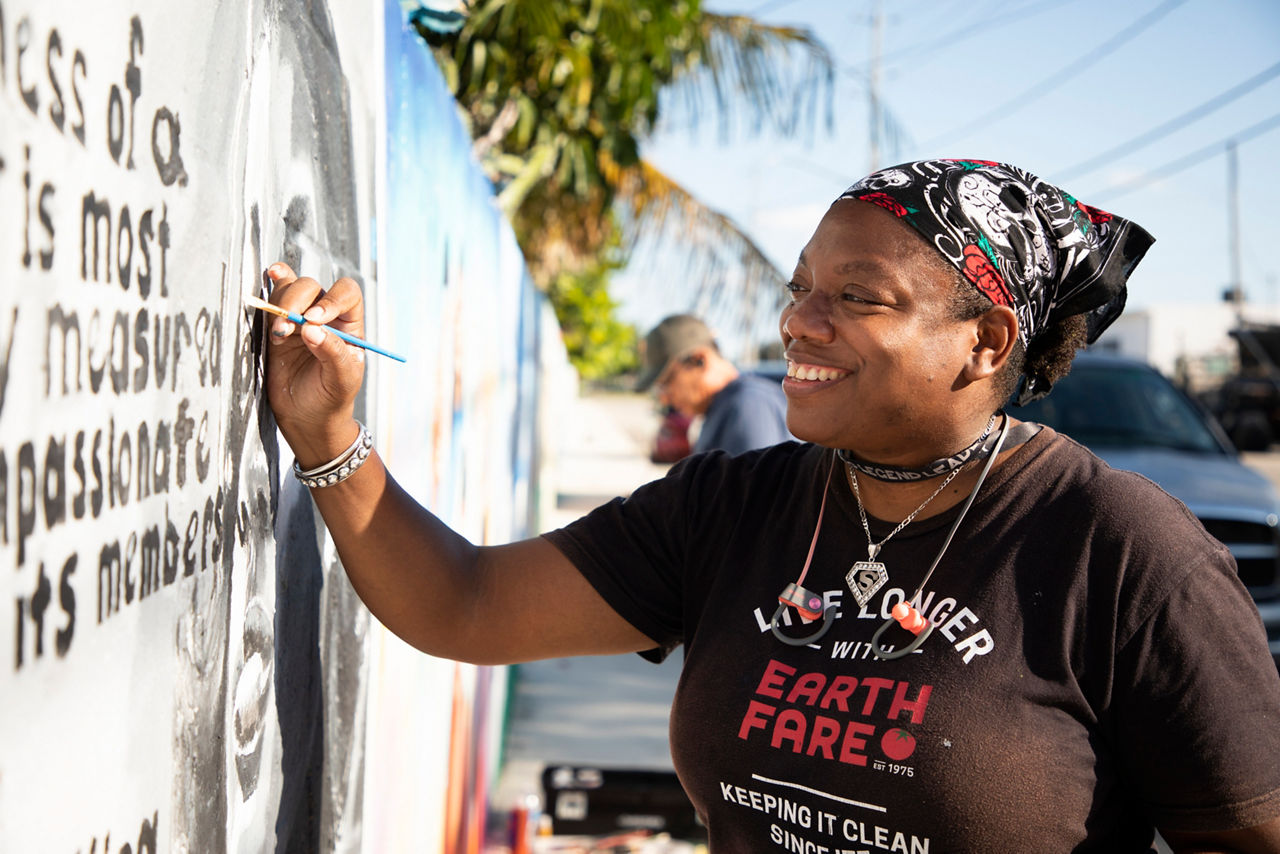 Dalhia Perryman (artist) paints at the Unity Wall. A wall that formerly served as a symbol of division is now a beacon of light for inclusion and diversity in Lake Worth Beach. The wall served as an unofficial border between the residents of the "Osborne Colored Addition" and their white neighbors. The city's zoning code required Black residents to live in the Osborne subdivision until 1969. 67 South Florida professional artists and residents helped paint the 1,175 foot long wall with art murals that represent the past, present, and future of the community.