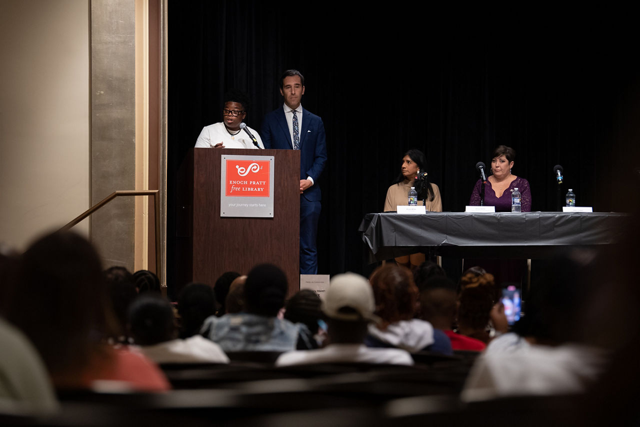 Tiffinnee Scott, community organizer and Maryland Peer Advisory Council member, speaks at the podium during a Town Hall meeting at the Enoch Pratt Free Library to discuss Baltimore’s response to the opioid crisis. Also on stage, from left, are Baltimore city Councilman Zeke Cohen, Lt. Governor Aruna Miller and Emily Keller, Maryland state Special Secretary of Opioid Response.