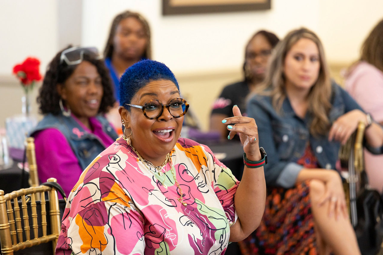 A person with short blue hair wearing scrubs is speaking in a facilitated discussion.