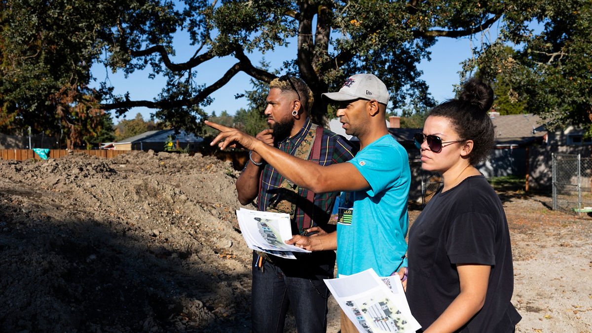 Housing developer Jessie Baines of Pierce County Land Trust and Black Home Initiative shows his wife Drea Bell and colleague Dawa'son Goes Behind the plans for a future 12 unit housing complex on land his family owns behind his home in Tacoma, Washington on October 5, 2023.