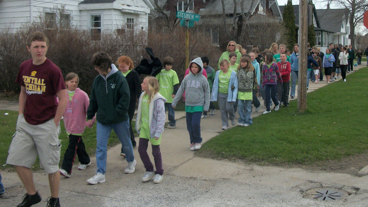Students and teachers walking to school using a sidewalk.