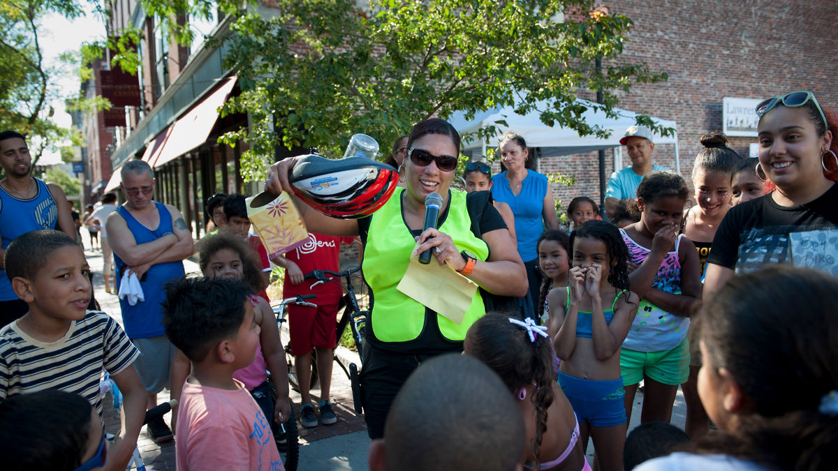 Community leader Vilma Lora conducts the Ciclovia raffle, in which the town gifted people with helmets and bikes. 2015 CULTURE OF HEALTH PRIZE.
