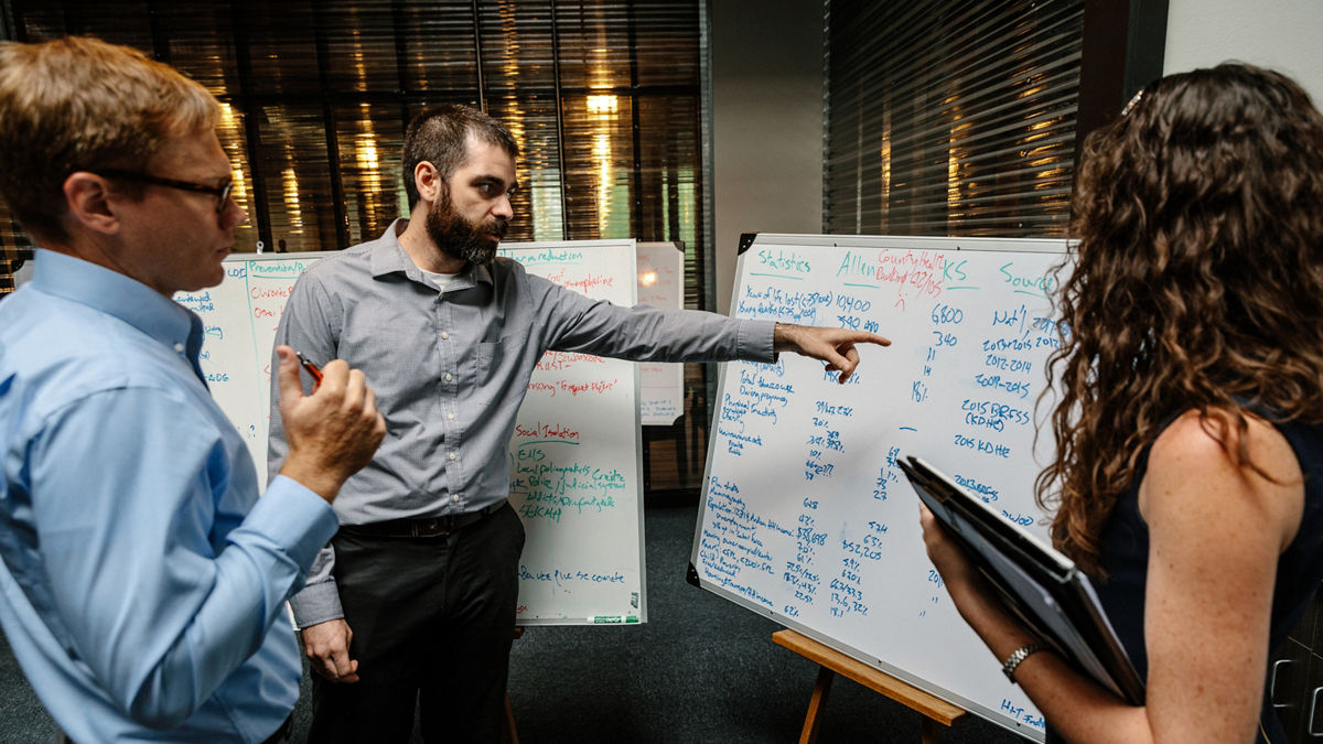 Iola, KS - August 1, 2017 - Ben Alexander, Deputy Director of THRIVE Allen County, points to statistical data on a marker board as his colleagues David Toland and Lisse Regehr look on.