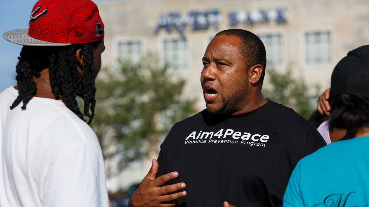 Rashid Junaid talks with a community member at an Aim4Peace barbecue in Kansas City, MO. Junaid is a violence prevention manager with Aim4Peace, which takes a public health approach to violence, treating it like a disease that spreads and must be contained. The intervention teams go into the community and the hospitals to work directly with at-risk individuals, friends and families.