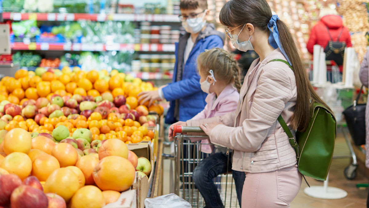 Mom with children in protective masks choose fruits to buy in the store.