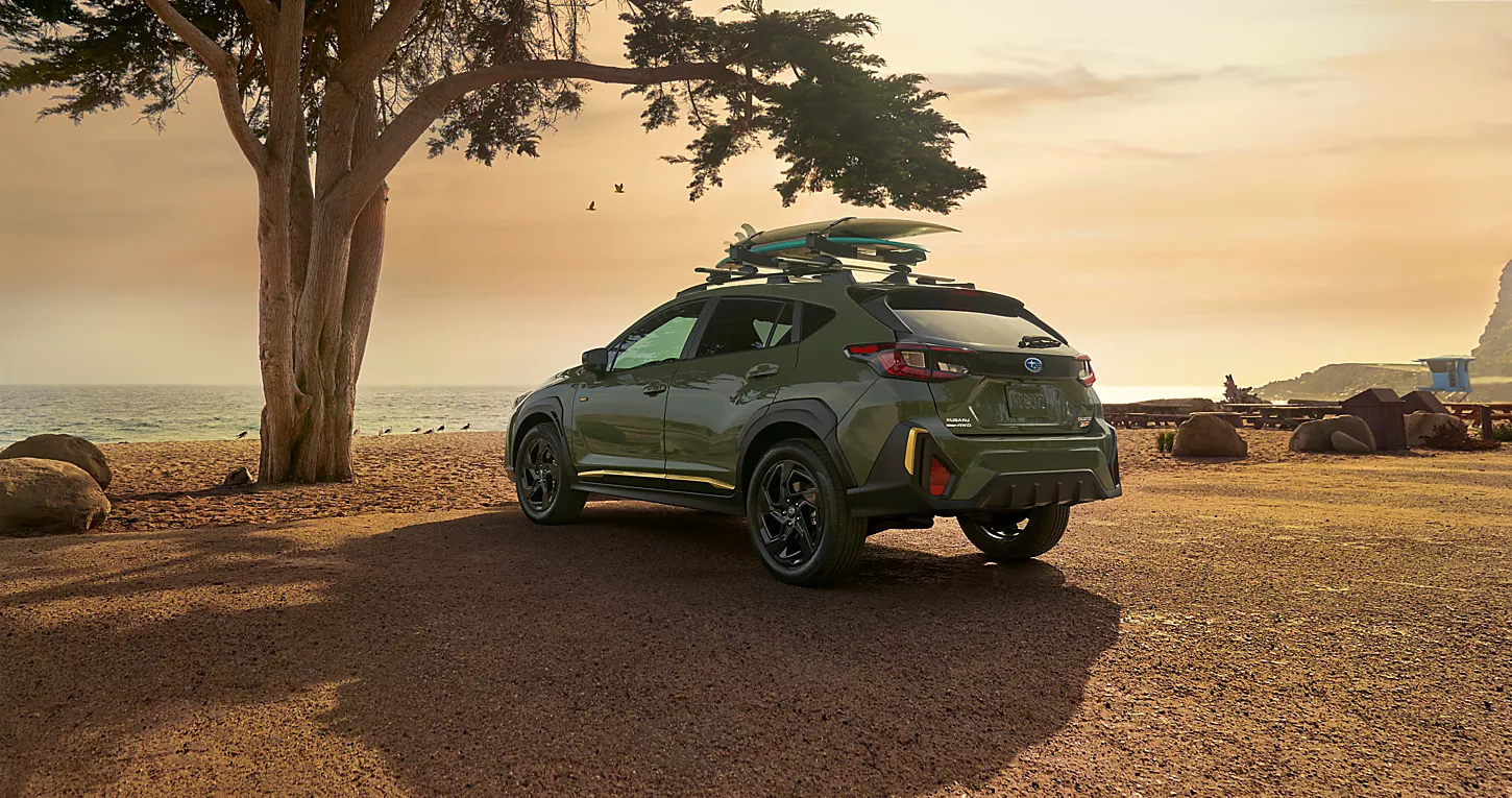 2024 Subaru Crosstrek parked by a beach with surfboards strapped on the hood