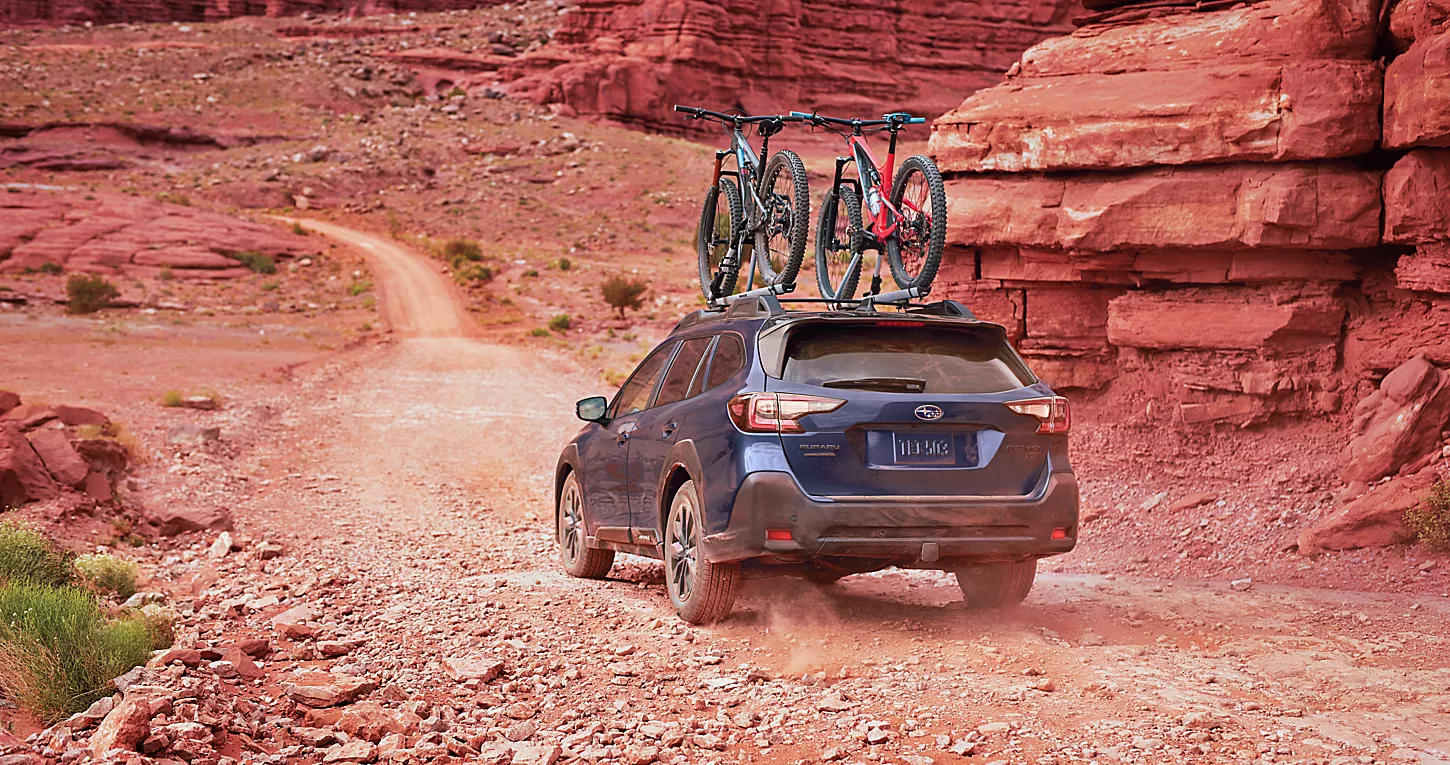 2023 Subaru Outback driving on a dirt road with two bicycles attached to its roof